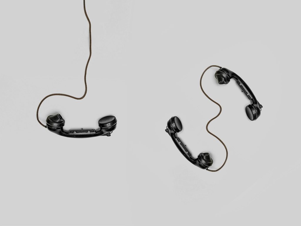 Zwei schwarze Vintage-Telefonhörer, die durch Kabel auf grauem Hintergrund verbunden sind.
